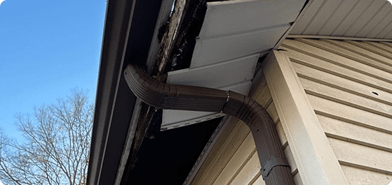 Damaged rain gutter with brown downspout on white siding